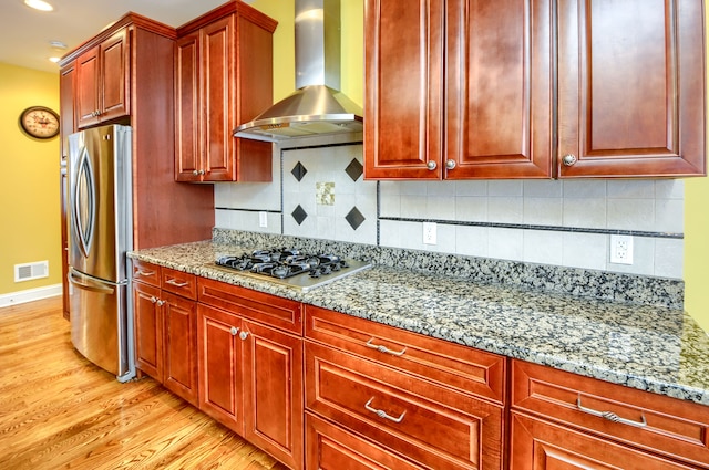 kitchen featuring light stone counters, tasteful backsplash, light hardwood / wood-style flooring, wall chimney range hood, and appliances with stainless steel finishes