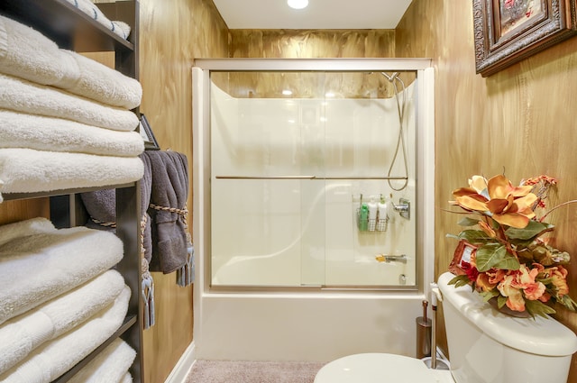 bathroom with combined bath / shower with glass door, wood walls, and toilet