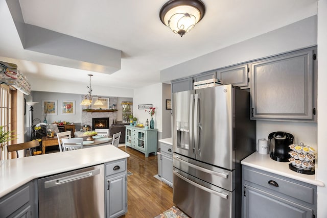 kitchen with dark hardwood / wood-style flooring, appliances with stainless steel finishes, gray cabinetry, and a stone fireplace