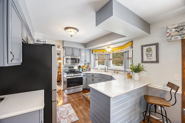 kitchen featuring a breakfast bar area, appliances with stainless steel finishes, gray cabinetry, kitchen peninsula, and dark hardwood / wood-style floors