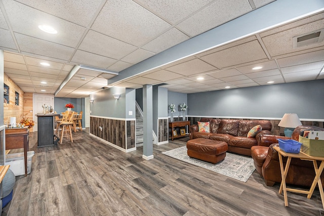 living room with a paneled ceiling, wood walls, and wood-type flooring