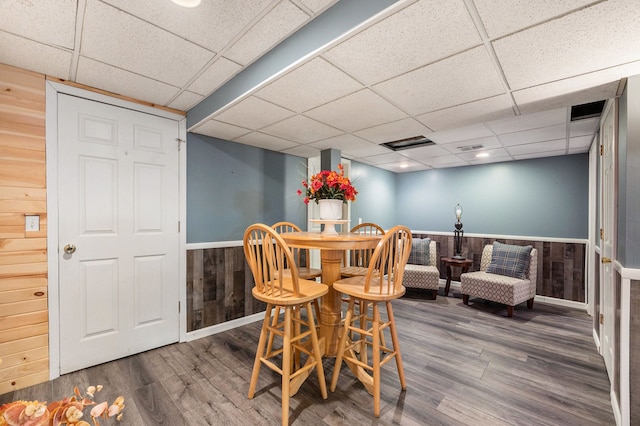 dining space with hardwood / wood-style flooring, wood walls, and a paneled ceiling