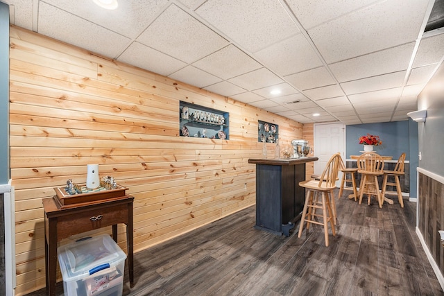 bar featuring dark hardwood / wood-style flooring, wood walls, and a drop ceiling