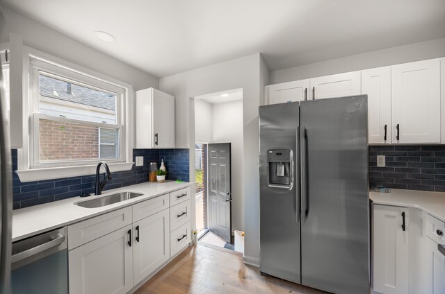 kitchen with stainless steel appliances, sink, white cabinets, light wood-type flooring, and tasteful backsplash