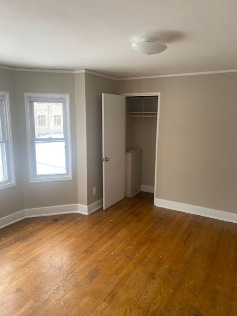 unfurnished bedroom with ornamental molding, a closet, and hardwood / wood-style flooring