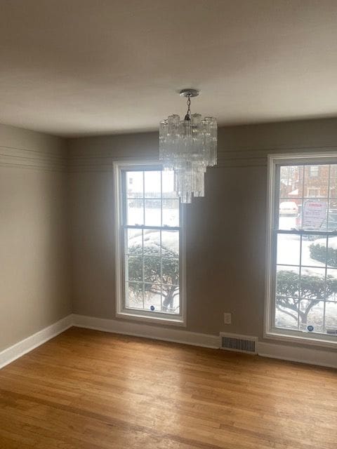 unfurnished dining area with light wood-type flooring, an inviting chandelier, and plenty of natural light