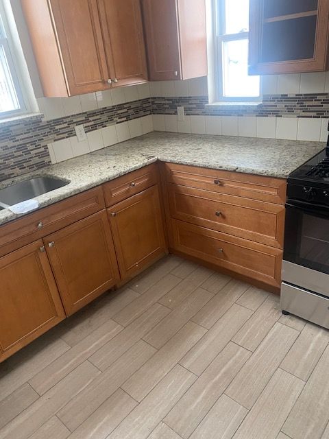 kitchen with stainless steel gas stove, light wood-type flooring, light stone counters, decorative backsplash, and sink