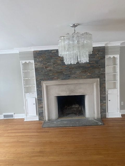 room details with a large fireplace, an inviting chandelier, crown molding, and wood-type flooring