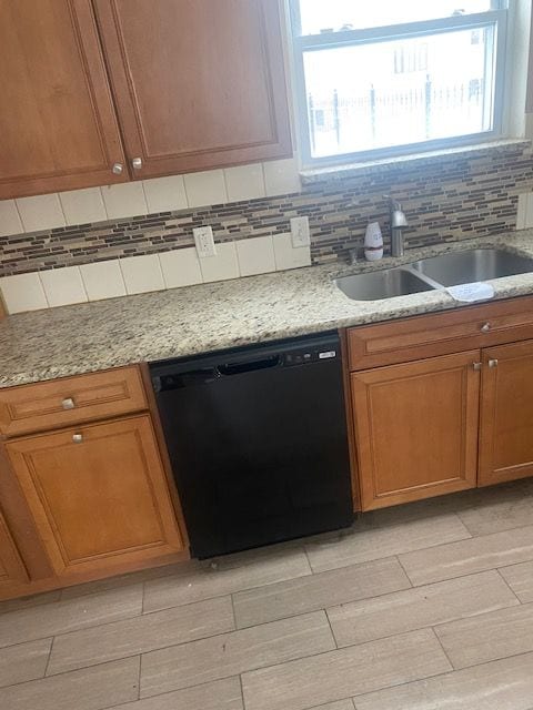 kitchen featuring sink, black dishwasher, backsplash, and light stone countertops