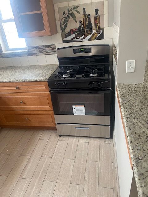 kitchen with light wood-type flooring, stainless steel gas range, and light stone counters