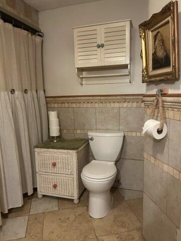 bathroom with toilet and tile walls