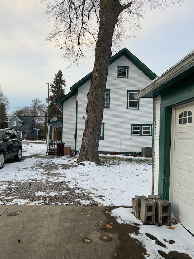 view of snow covered exterior featuring cooling unit and a garage