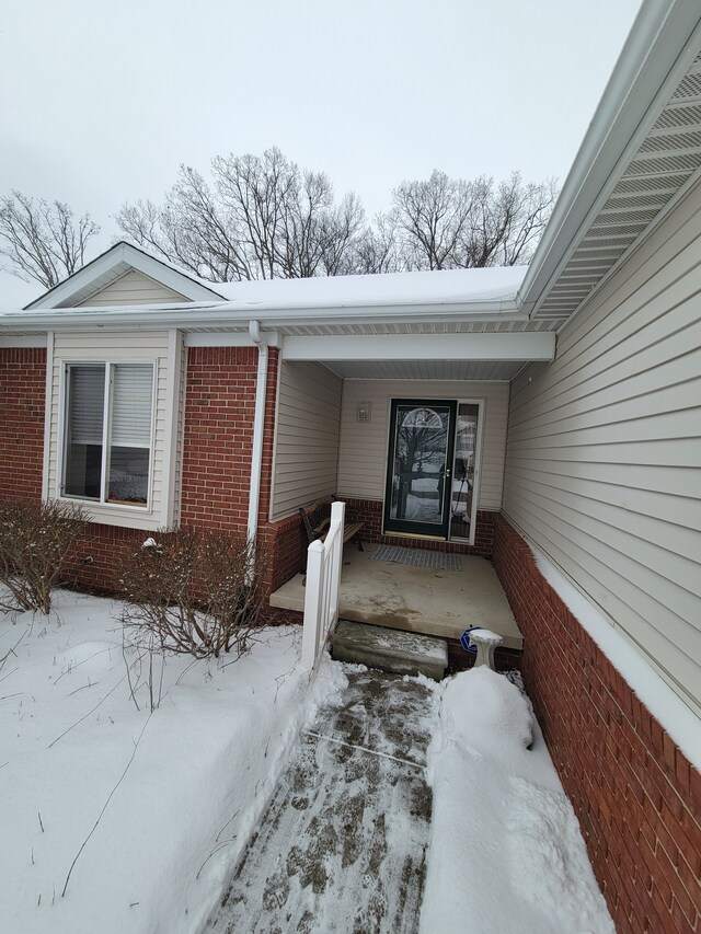 snow covered property entrance with brick siding and covered porch