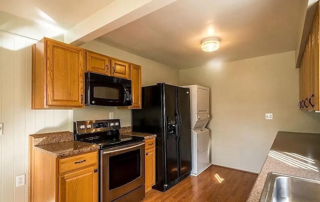 kitchen featuring black appliances, stacked washer and clothes dryer, dark stone countertops, and dark hardwood / wood-style floors