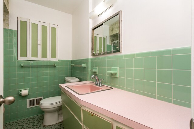 bathroom featuring toilet, tile patterned floors, vanity, and tile walls