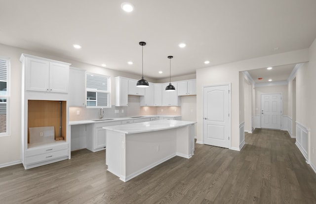 kitchen with dark wood-type flooring, a sink, a kitchen island, white cabinetry, and light countertops