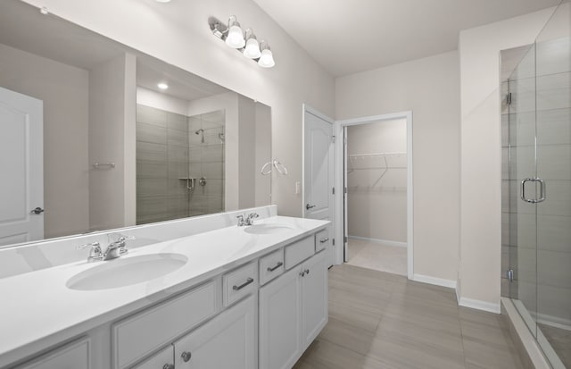 bathroom featuring a spacious closet, double vanity, a sink, and a shower stall