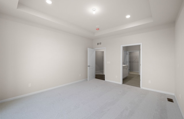 unfurnished bedroom featuring a spacious closet, a closet, light carpet, and a tray ceiling