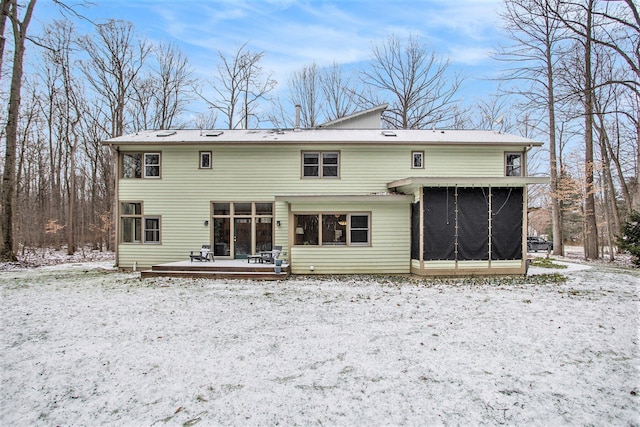 snow covered house featuring a wooden deck and a sunroom