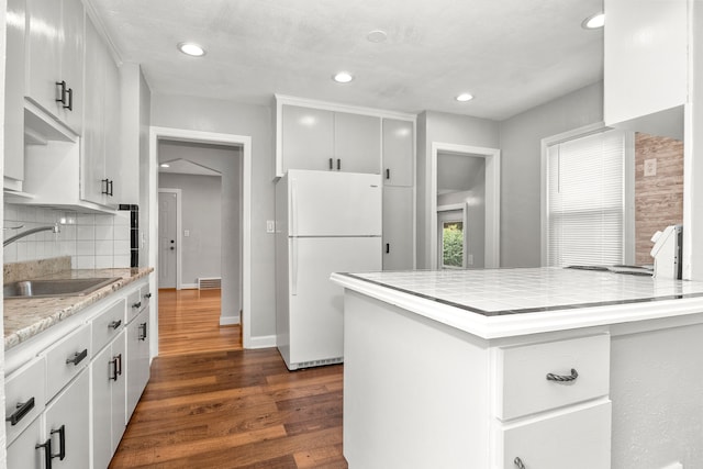 kitchen with white fridge, dark wood-type flooring, sink, white cabinetry, and backsplash