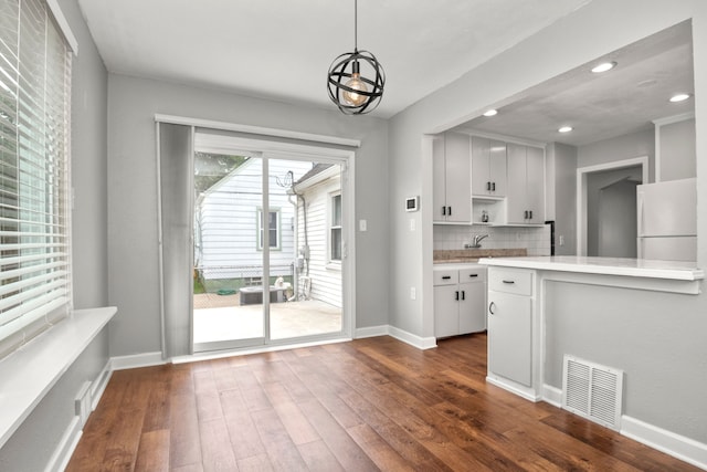 kitchen featuring white fridge, dark hardwood / wood-style flooring, white cabinetry, decorative light fixtures, and tasteful backsplash