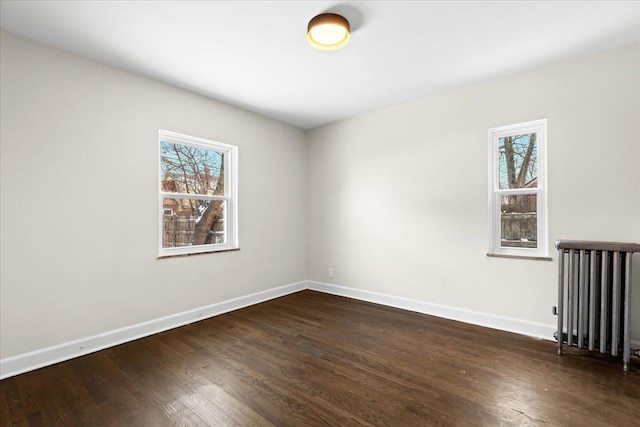 empty room featuring dark wood-type flooring, radiator heating unit, and a wealth of natural light