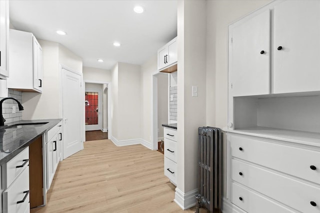 kitchen featuring sink, white cabinets, tasteful backsplash, light hardwood / wood-style flooring, and radiator