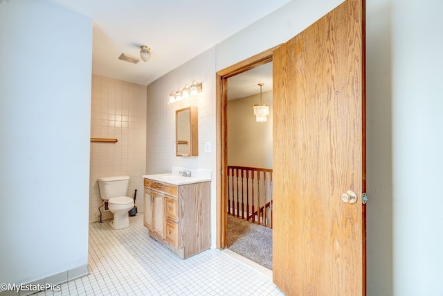 bathroom featuring toilet, vanity, tile walls, tile patterned floors, and an inviting chandelier