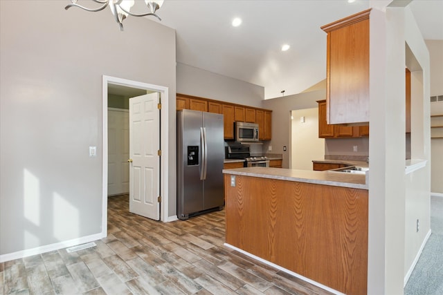 kitchen featuring an inviting chandelier, appliances with stainless steel finishes, kitchen peninsula, and light wood-type flooring