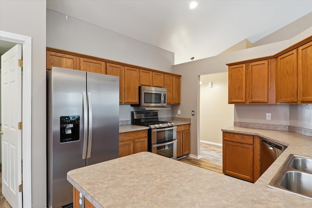 kitchen with sink, light hardwood / wood-style floors, appliances with stainless steel finishes, and lofted ceiling