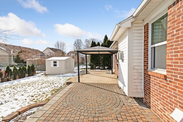 snow covered patio with a gazebo and a storage unit