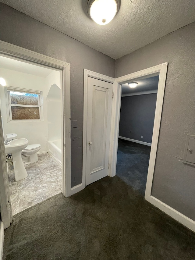 hallway featuring sink, a textured ceiling, and dark colored carpet