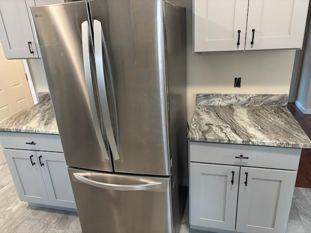 kitchen with white cabinetry, stainless steel refrigerator, and light stone counters