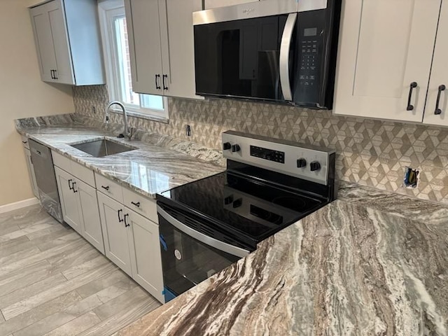 kitchen with appliances with stainless steel finishes, white cabinetry, light stone counters, and sink