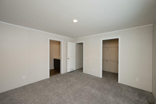 unfurnished bedroom featuring a closet, crown molding, a spacious closet, carpet flooring, and a textured ceiling