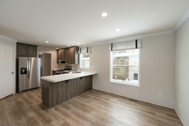 kitchen featuring appliances with stainless steel finishes, crown molding, kitchen peninsula, a kitchen bar, and dark brown cabinetry