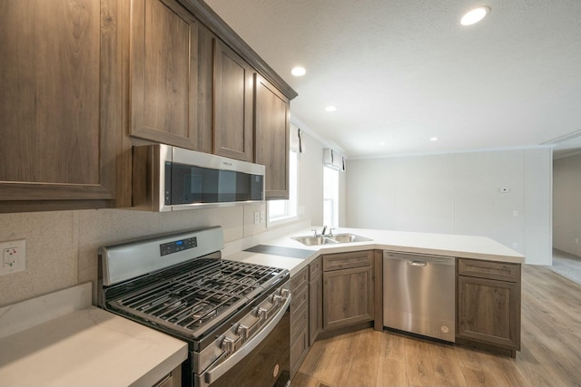 kitchen featuring stainless steel appliances, sink, ornamental molding, light hardwood / wood-style flooring, and kitchen peninsula