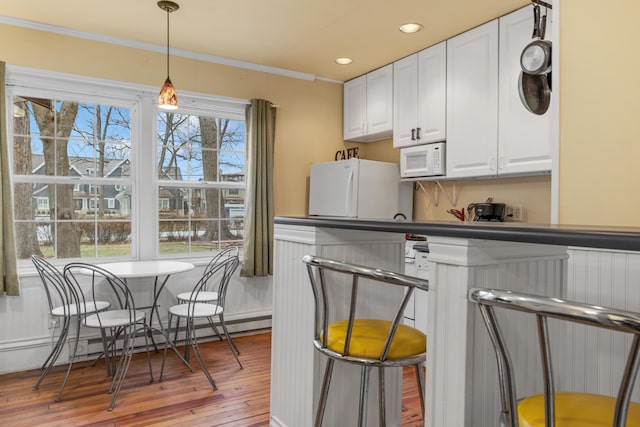 kitchen featuring white appliances, white cabinetry, ornamental molding, and hardwood / wood-style floors