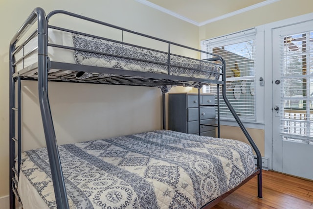 bedroom with a baseboard heating unit, hardwood / wood-style floors, and crown molding