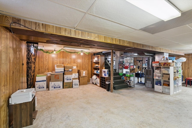 basement featuring a paneled ceiling, carpet, and wood walls