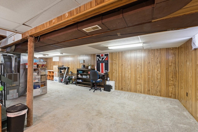 basement featuring a paneled ceiling, wooden walls, carpet floors, and heating unit