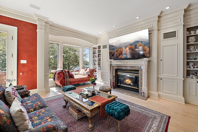 living room featuring built in shelves, light hardwood / wood-style flooring, ornate columns, and a premium fireplace