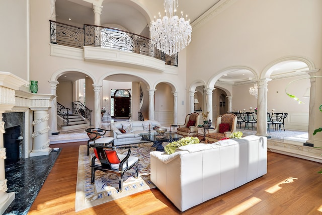 living room featuring ornate columns, hardwood / wood-style flooring, a high ceiling, a notable chandelier, and a high end fireplace