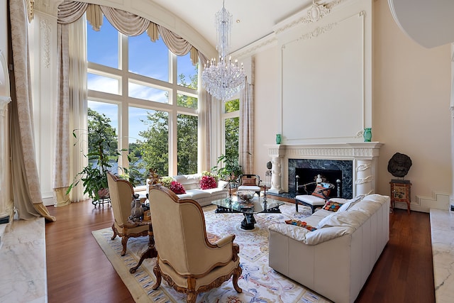 living room featuring a high end fireplace, an inviting chandelier, a towering ceiling, and hardwood / wood-style floors