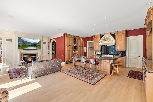 kitchen with light hardwood / wood-style floors, a kitchen breakfast bar, a fireplace, custom range hood, and a kitchen island