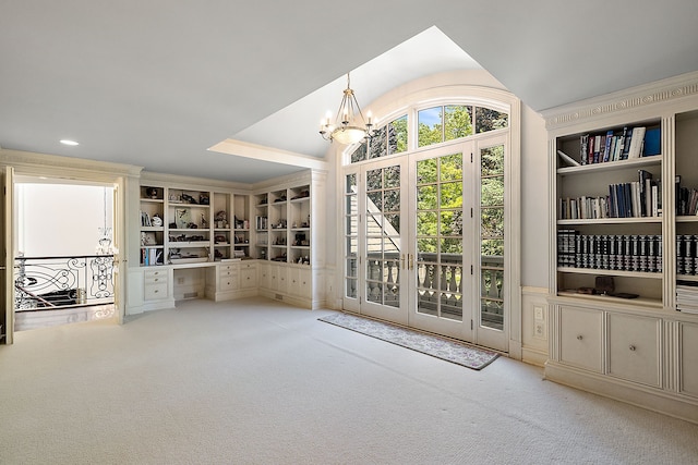 unfurnished living room featuring an inviting chandelier, built in features, lofted ceiling, and light colored carpet