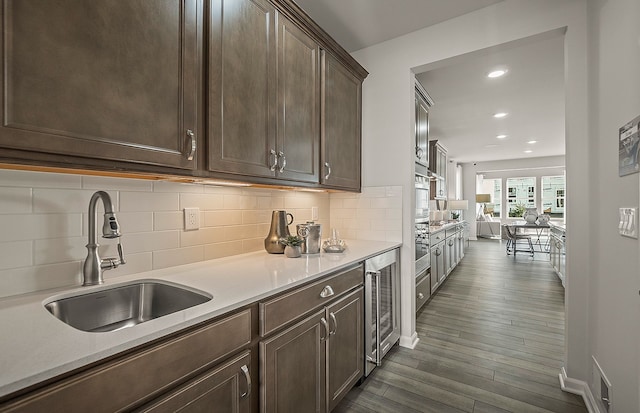 kitchen with sink, decorative backsplash, beverage cooler, dark brown cabinets, and dark wood-type flooring