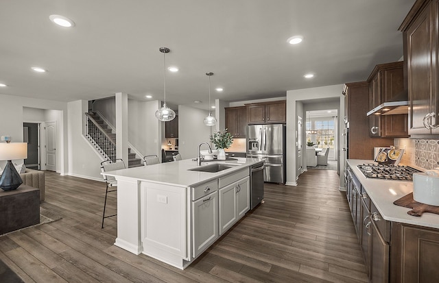 kitchen with a kitchen island with sink, appliances with stainless steel finishes, hanging light fixtures, decorative backsplash, and sink