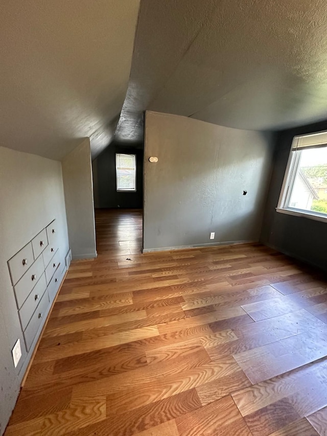 additional living space with lofted ceiling, light wood-type flooring, and a textured ceiling