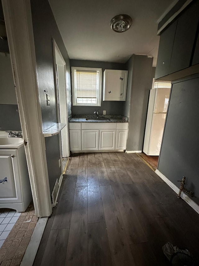 kitchen with sink, white fridge, white cabinetry, and wood-type flooring